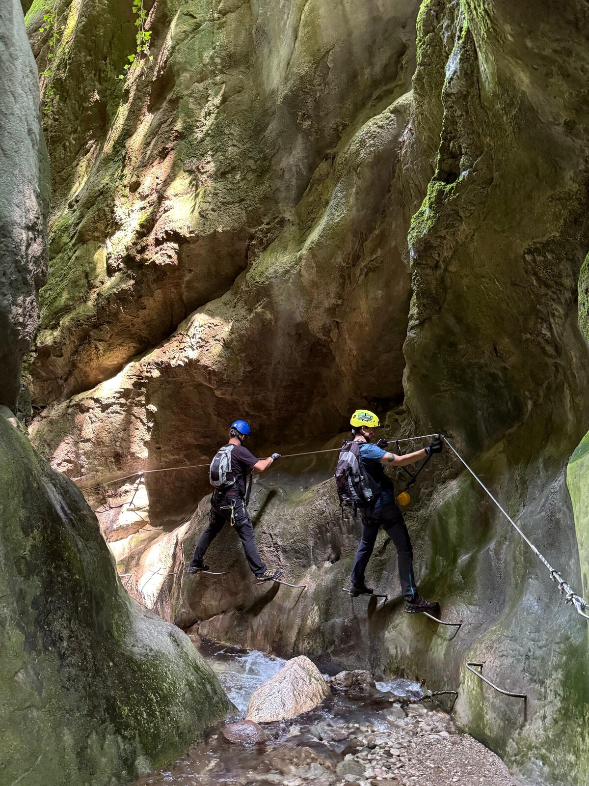 Two climbers traverse a narrow gorge above flowing water.