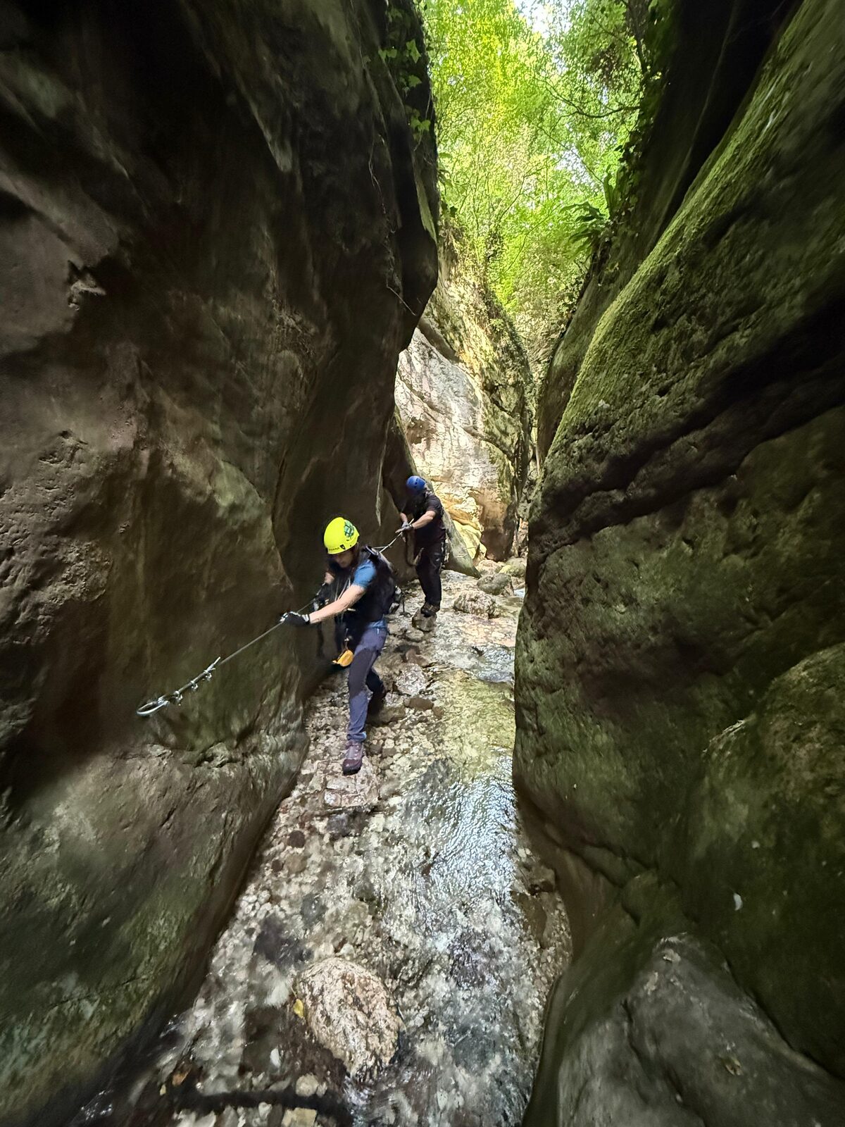 Two climbers follow the safety cable through a shaded gorge.