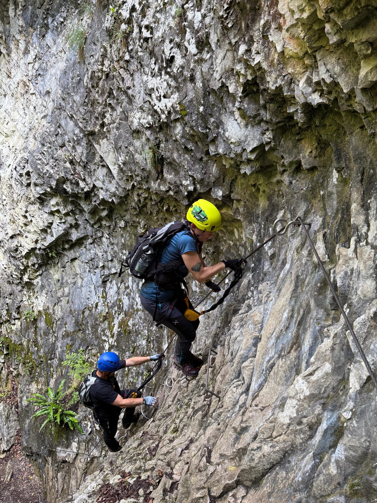 Two climbers move along a cable-protected rock face.